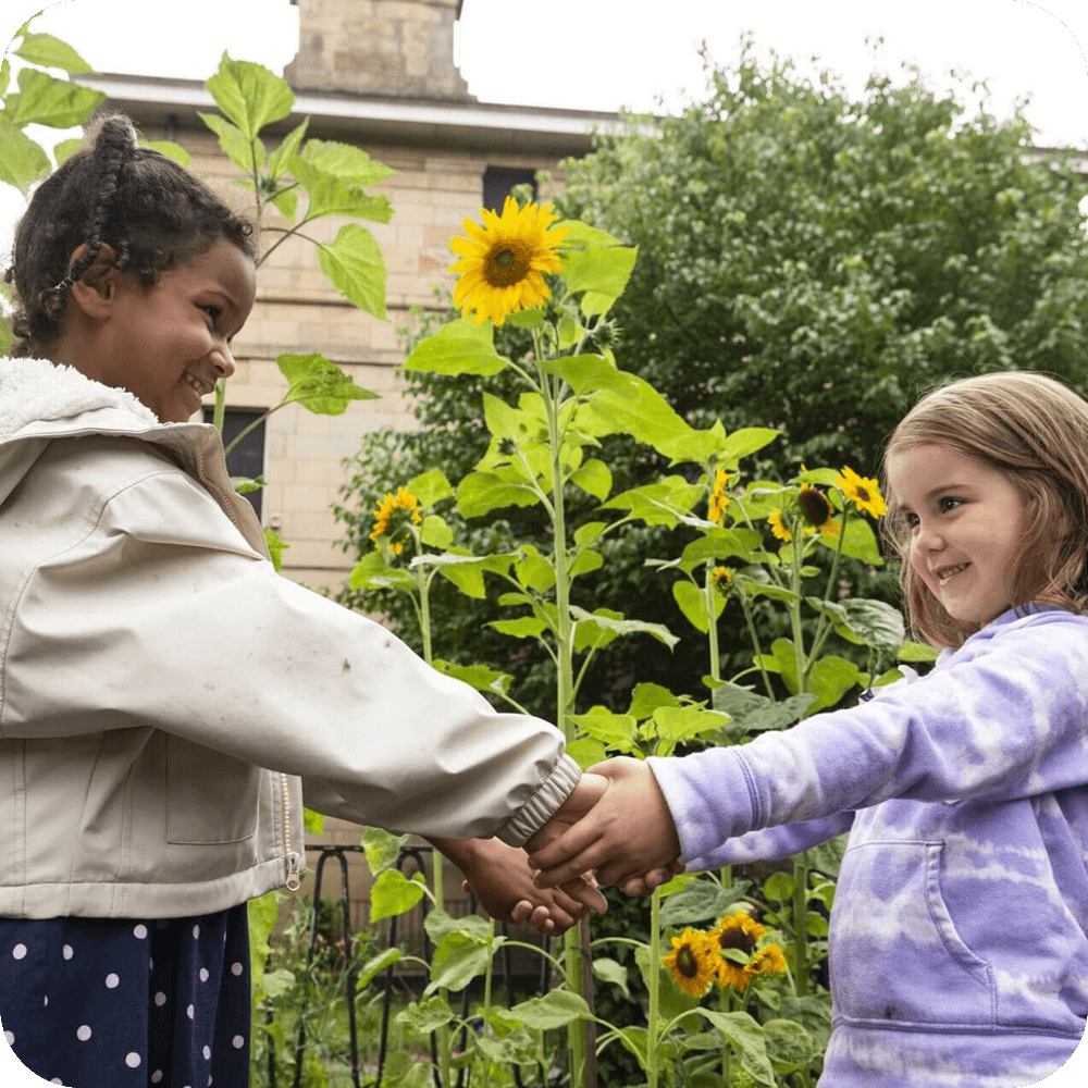 Two girls holding hands, in front of a sunflower