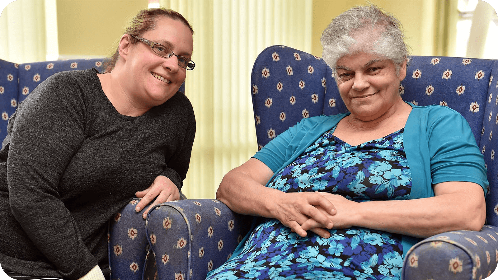 An older lady sat in an armchair, alongside a family member