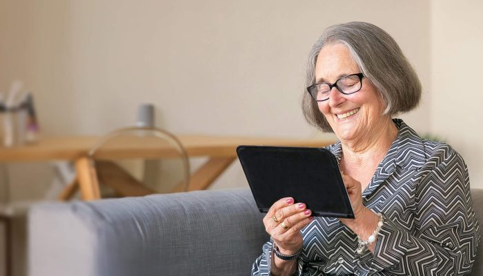 An older woman sitting on a sofa using a tablet